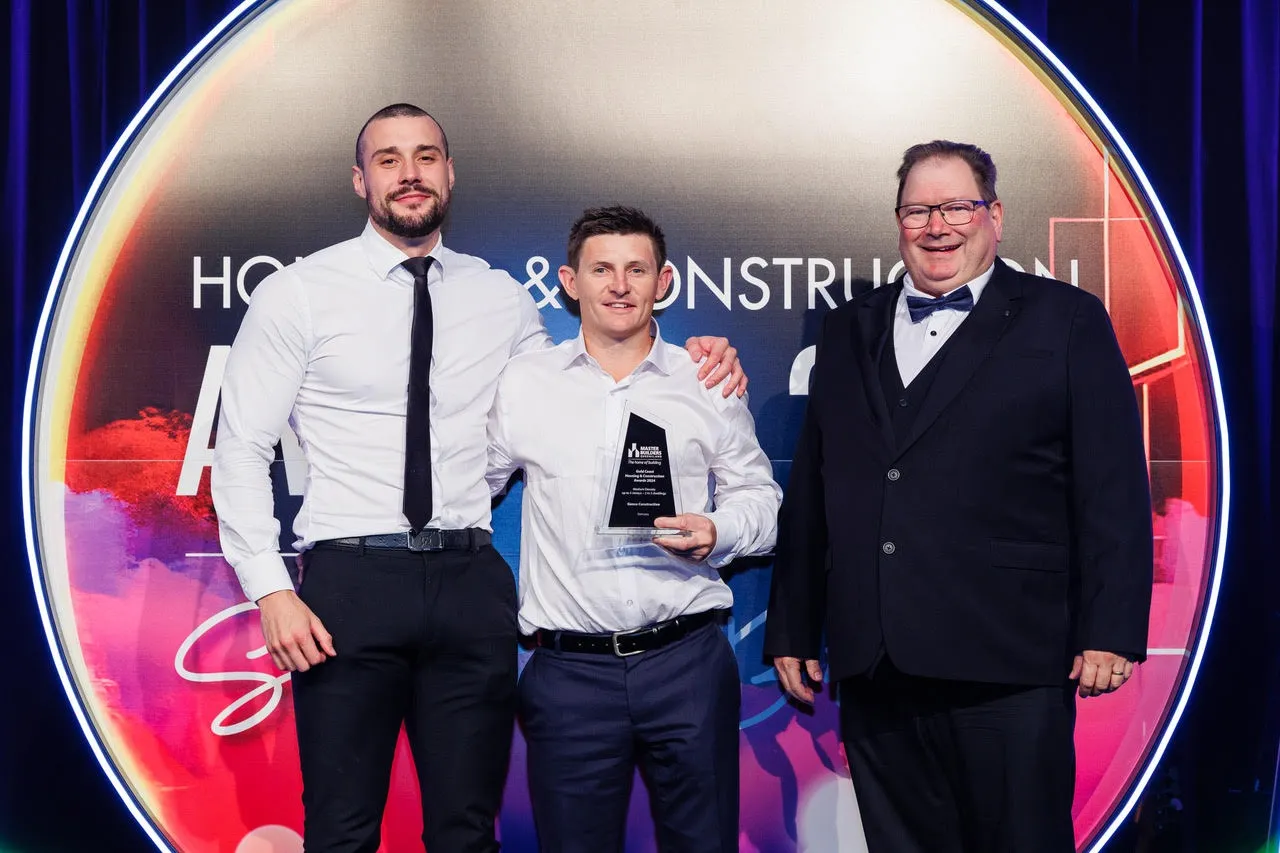 Elijah Turkovic, Genco Construction’s Cameron Bryant holding the glass Master Builders trophy, and the award presenter on stage