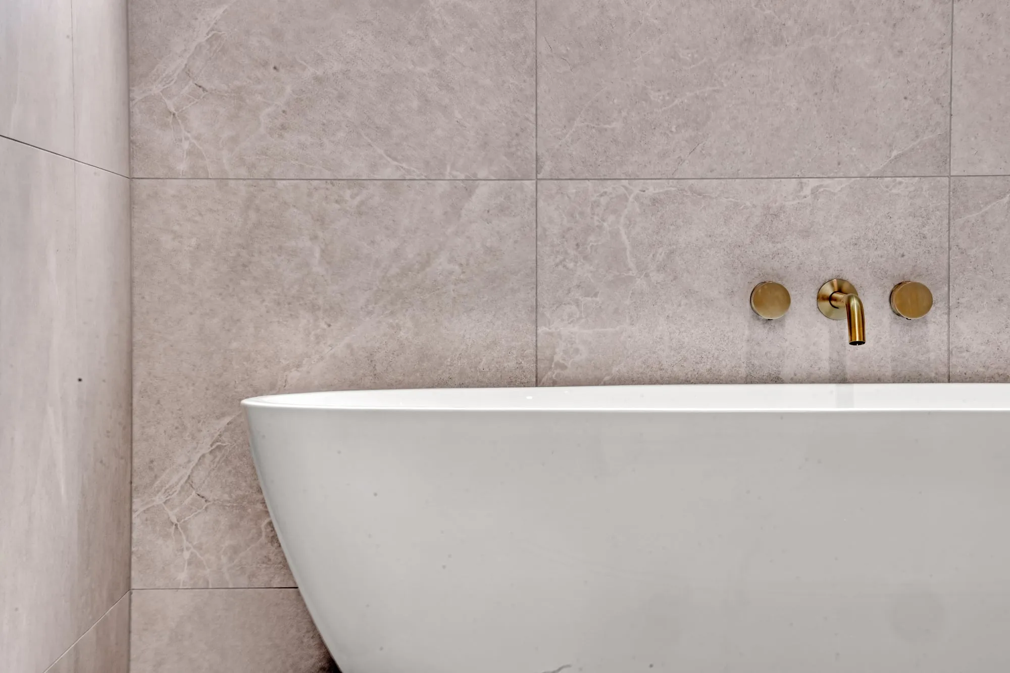 Freestanding bath with brass wall-mounted tapware against large stone-look tiles