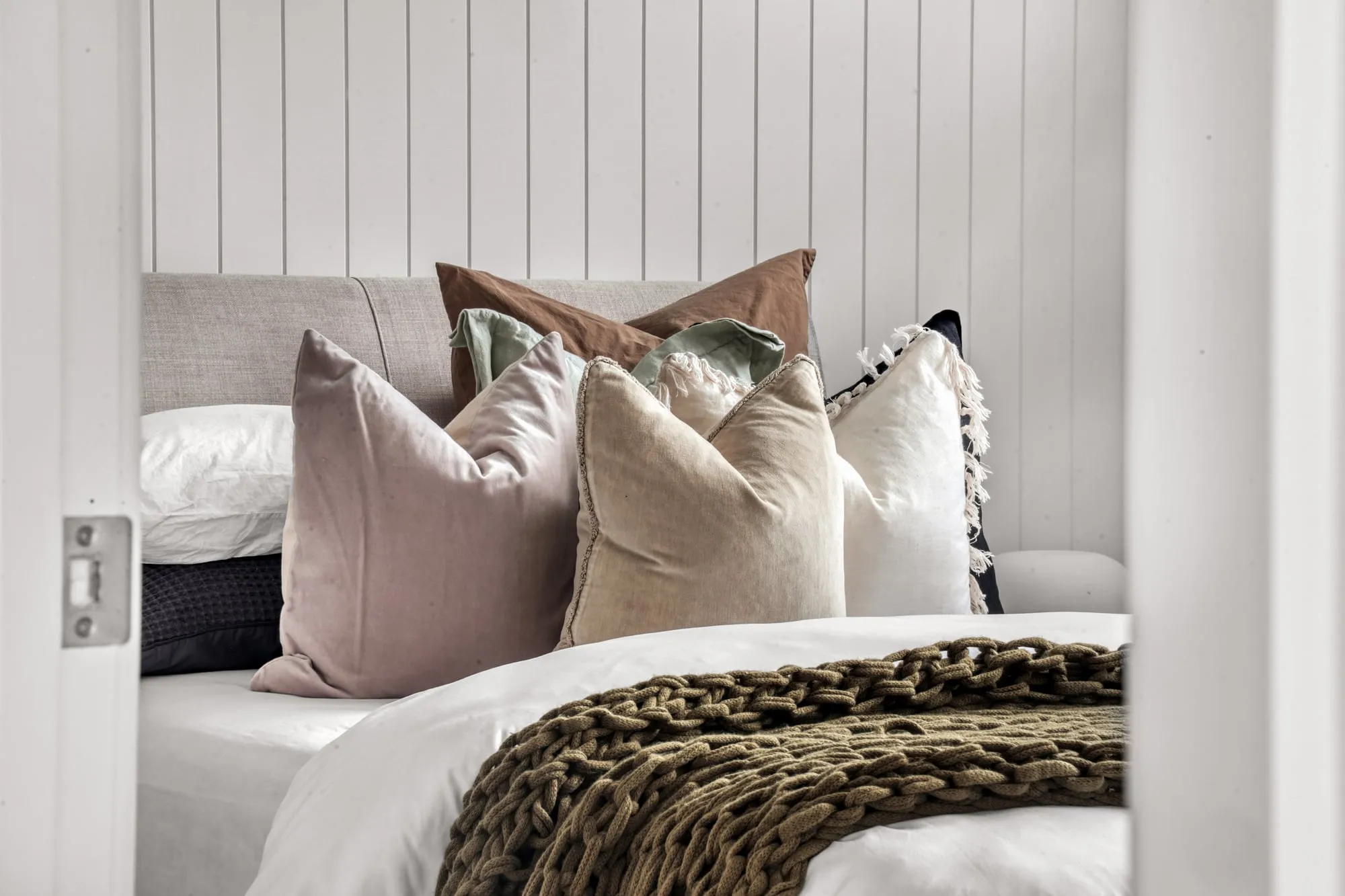 Bedroom with a panelled wall and layered cushions and throws