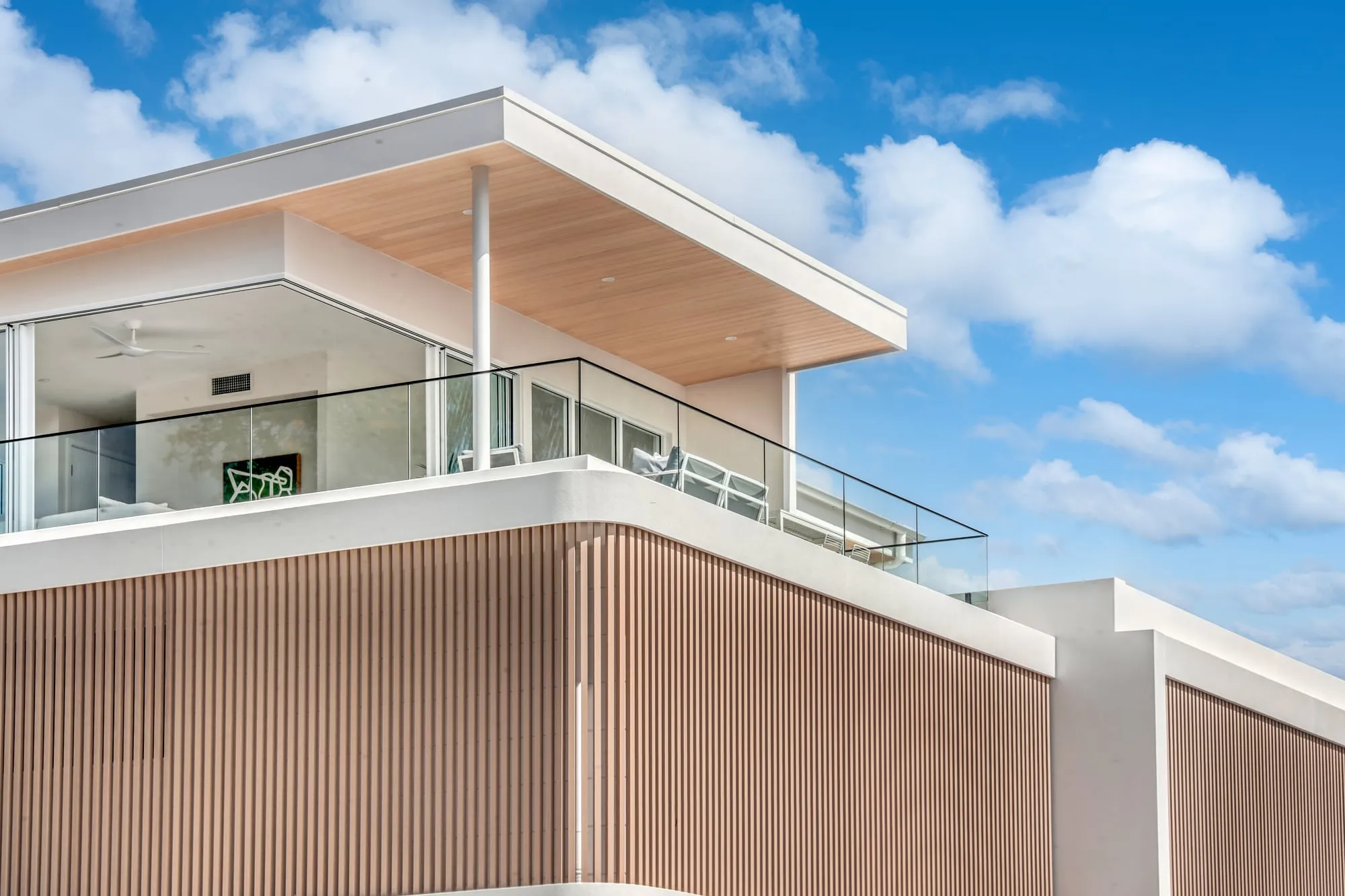 Upper-level balcony with a glass balustrade under a timber-lined roof overhang