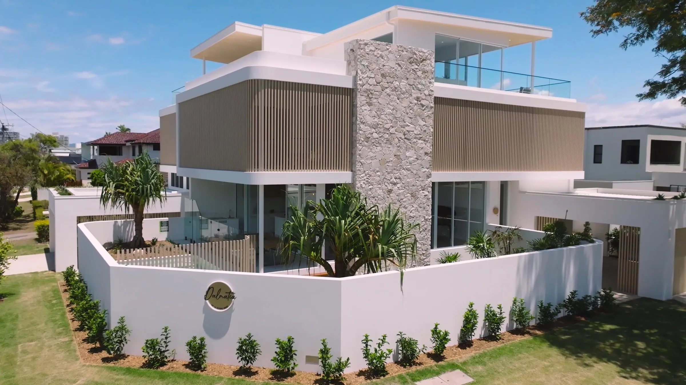 Dalmatia in Broadbeach Waters: a curved white upper floor with timber slats either side of a stone column, behind a white front wall bearing the Dalmatia sign