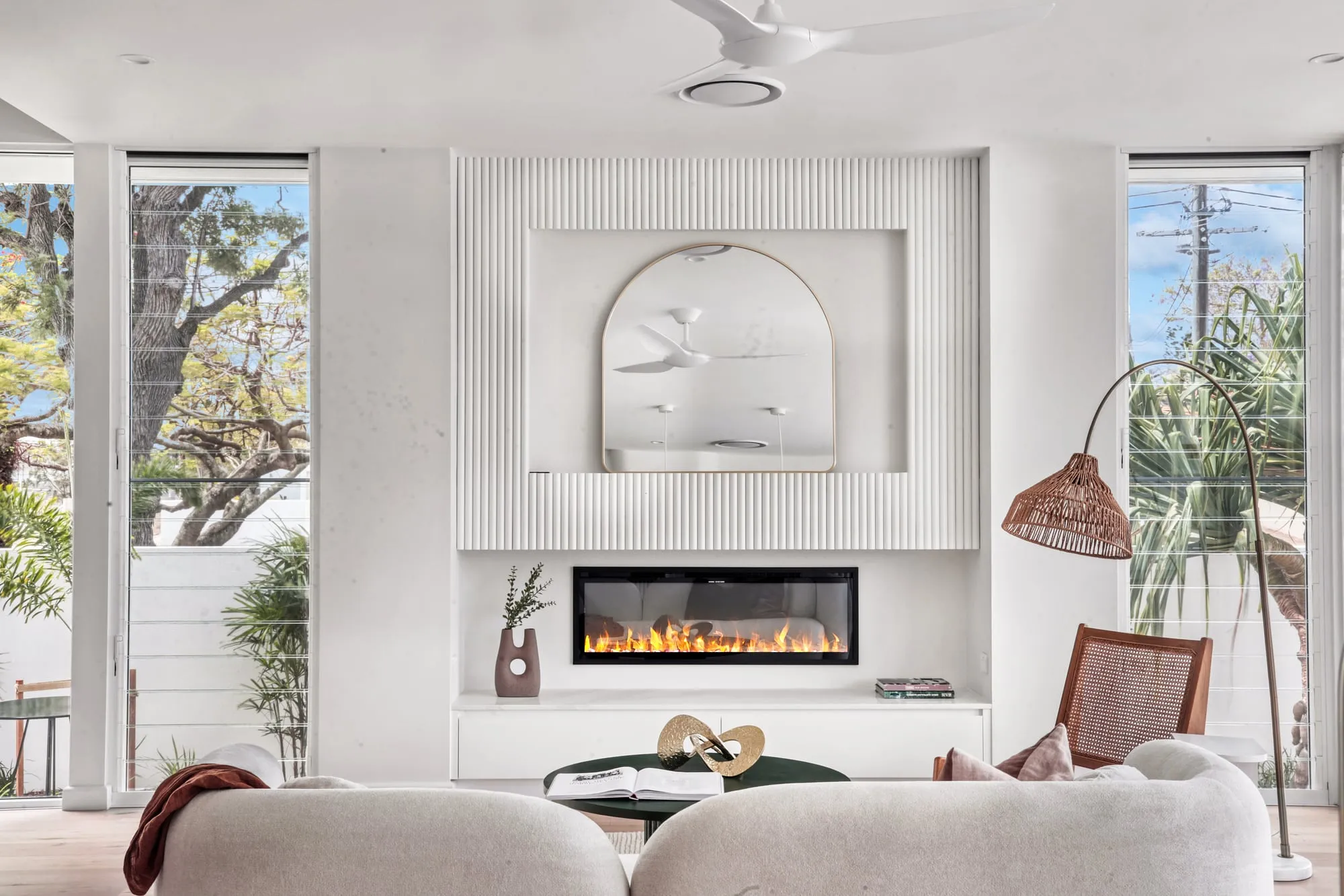 Living room with a fluted fireplace wall, a built-in fire and an arched mirror
