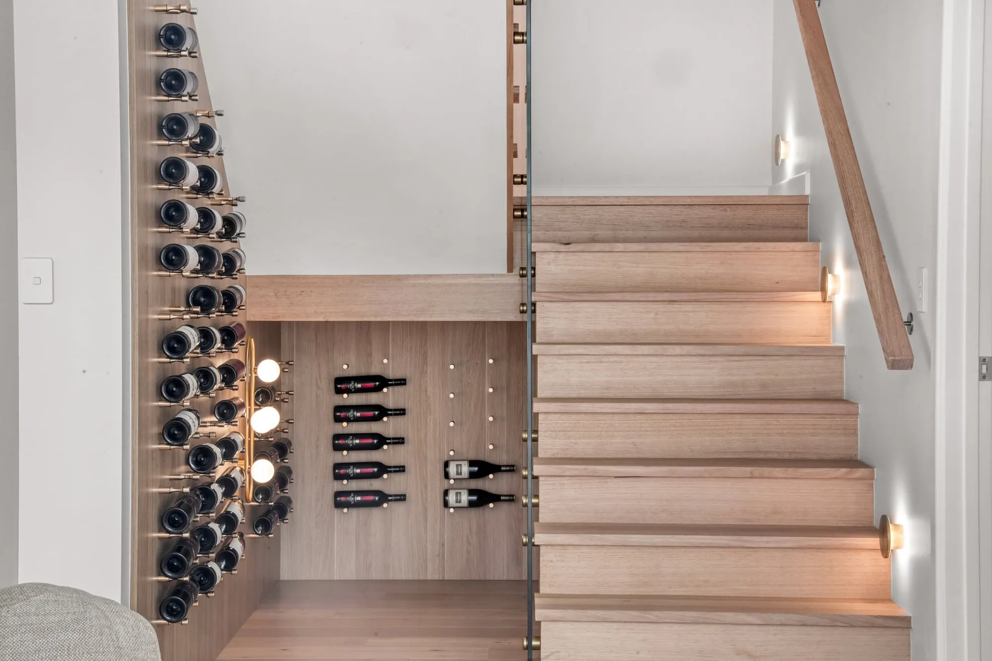 Wall-mounted wine display beside a timber staircase with step lights
